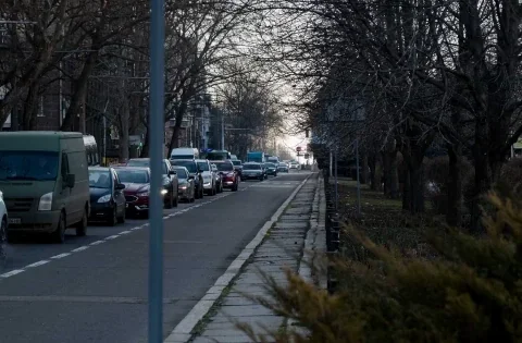 Черга легковиків і фургона на міській вулиці з деревами в сутінках
