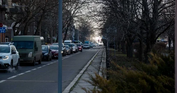 Черга легковиків і фургона на міській вулиці з деревами в сутінках