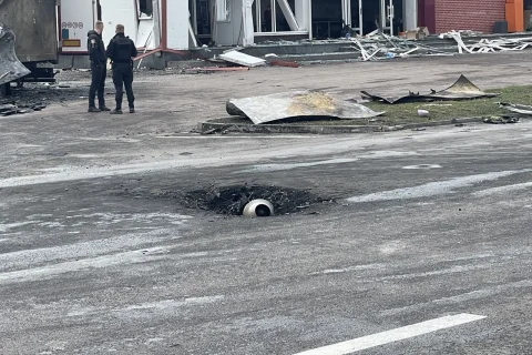 Вирва в асфальті з круглим уламком, двоє поліцейських біля пошкодженої будівлі